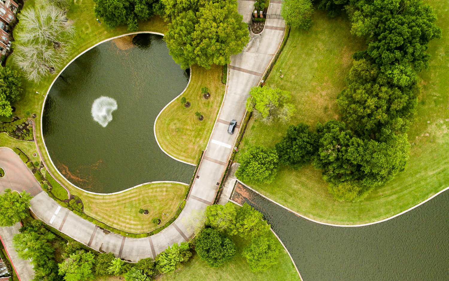 Top-down aerial photo of the lake at Meyerland Park, showing the driveway entrance into a waterfront apartment complex.