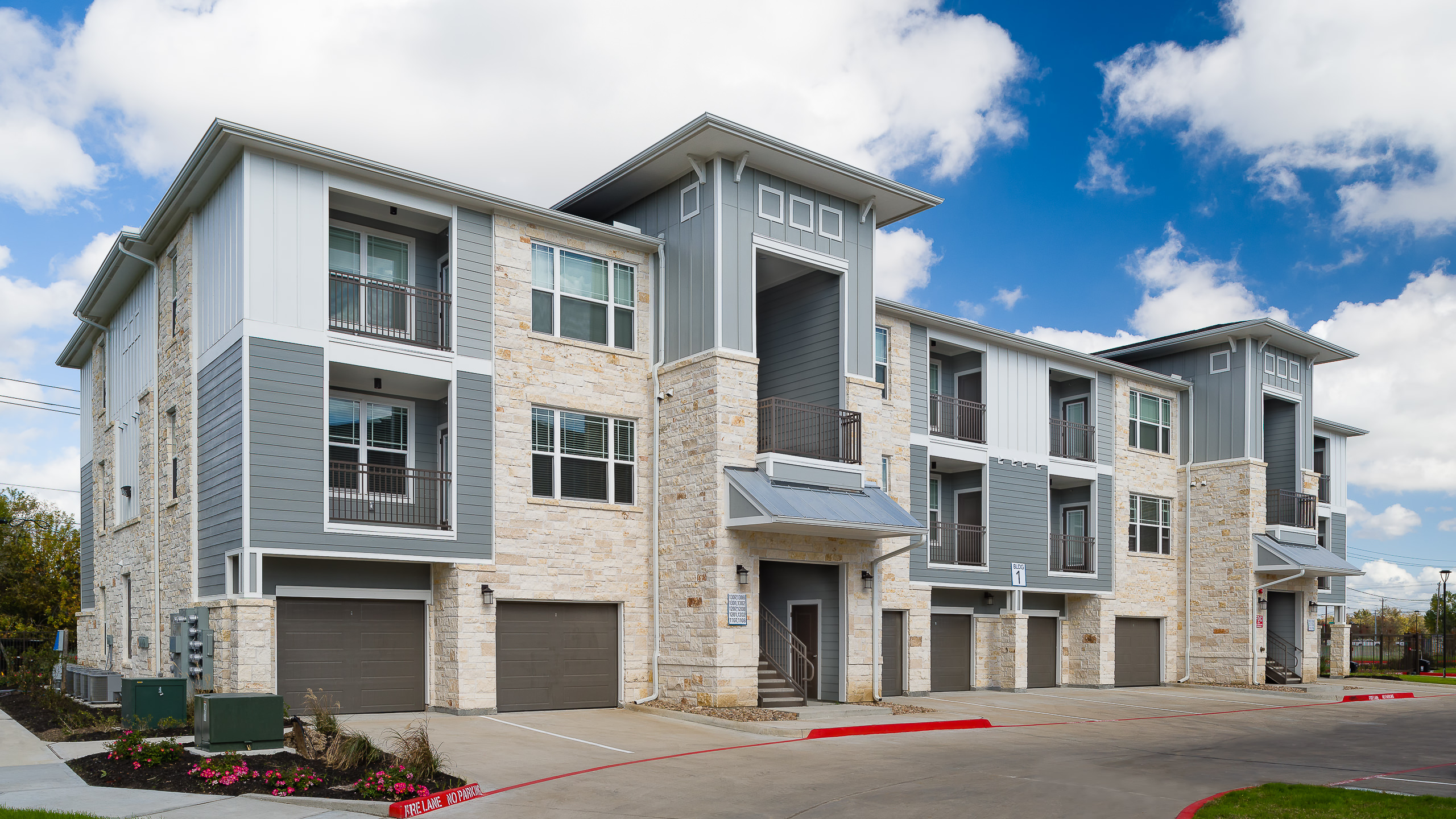 Exterior architectural photo of a Houston apartment building, featuring a natural stone facade with modern blue design accents.