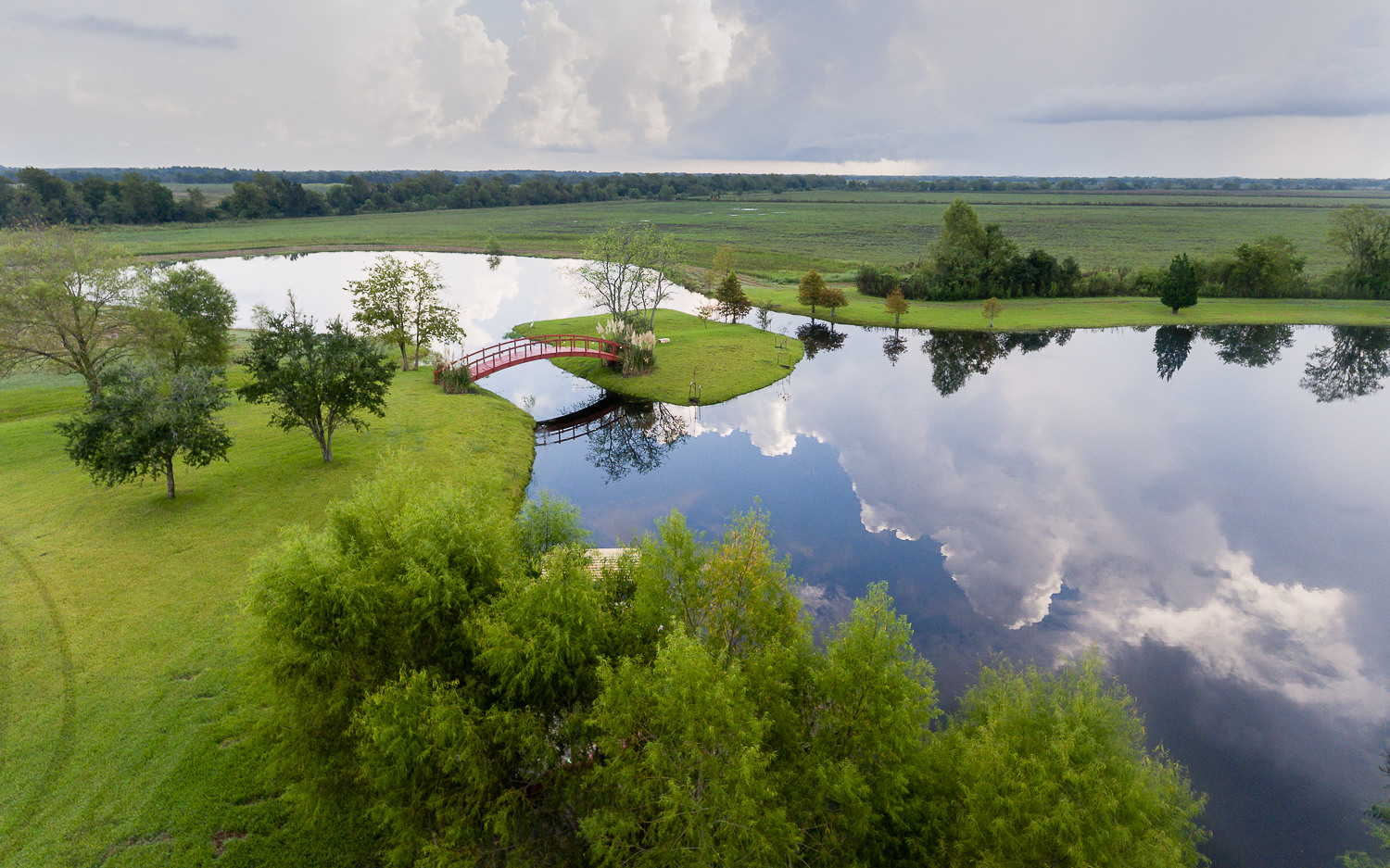 Drone photo of a scenic lake in Sealy, TX. The image captures a bridge, an island, and the sky reflecting on the water's surface.