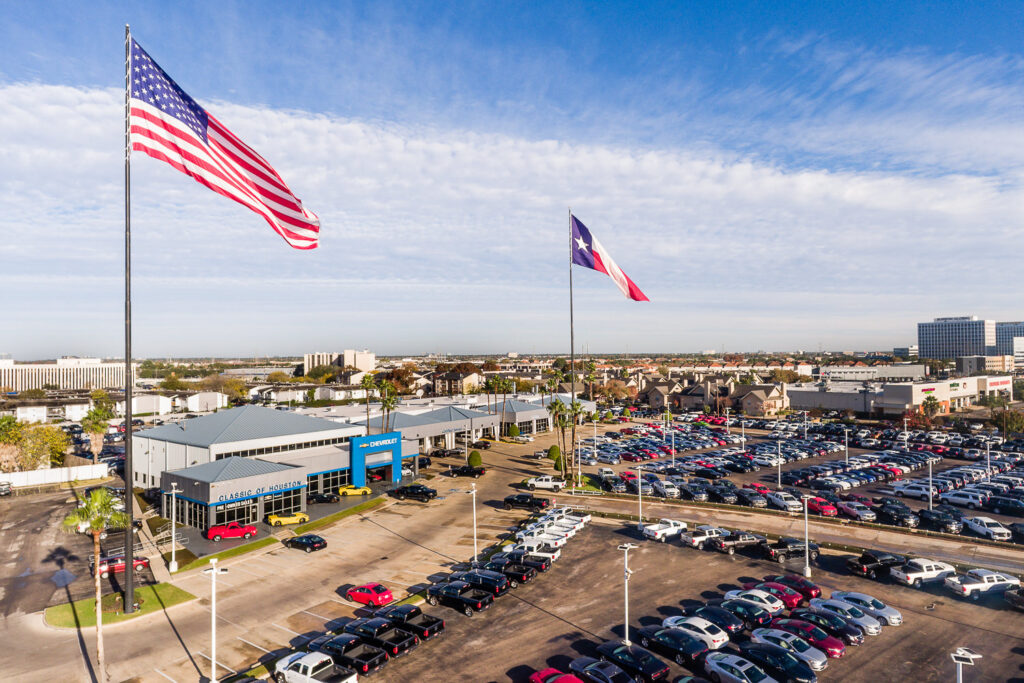 Aerial drone photo of a Chevrolet dealership in Southwest Houston. Large flags fly over the expansive commercial car lot.