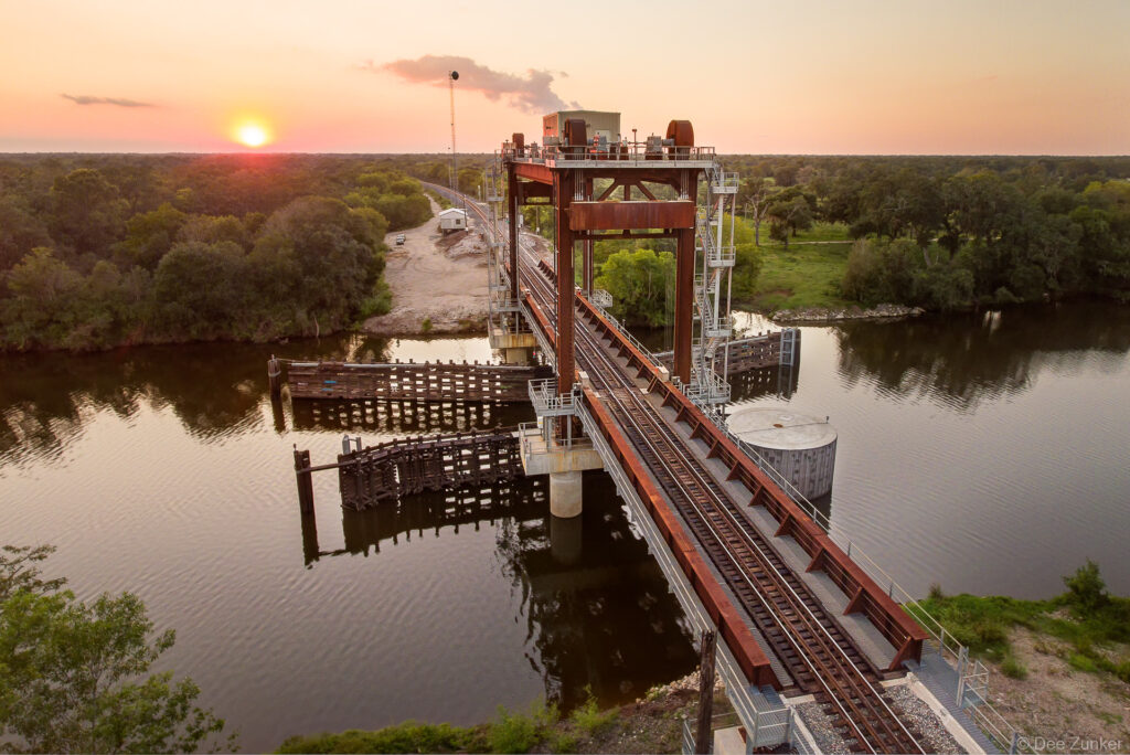 Aerial drone view of the San Bernard River vertical-lift train bridge at sunset, highlighting the industrial infrastructure.