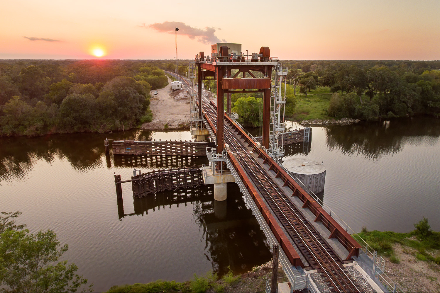 Aerial drone view of the San Bernard River vertical-lift train bridge at sunset, highlighting the industrial infrastructure.
