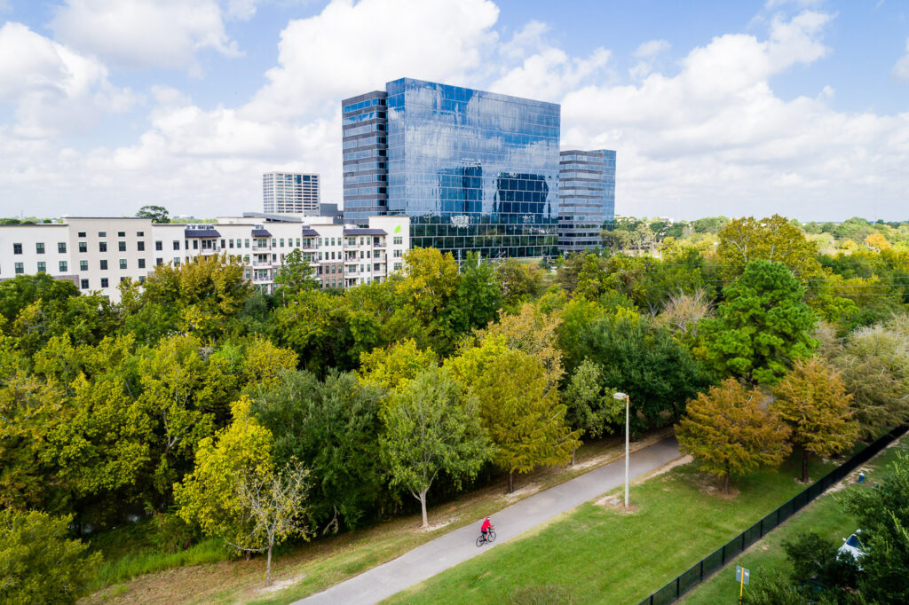 Sunlit, paved running and biking trails winding through the green landscape of Terry Hershey Park in Houston's Energy Corridor on a sunny day.