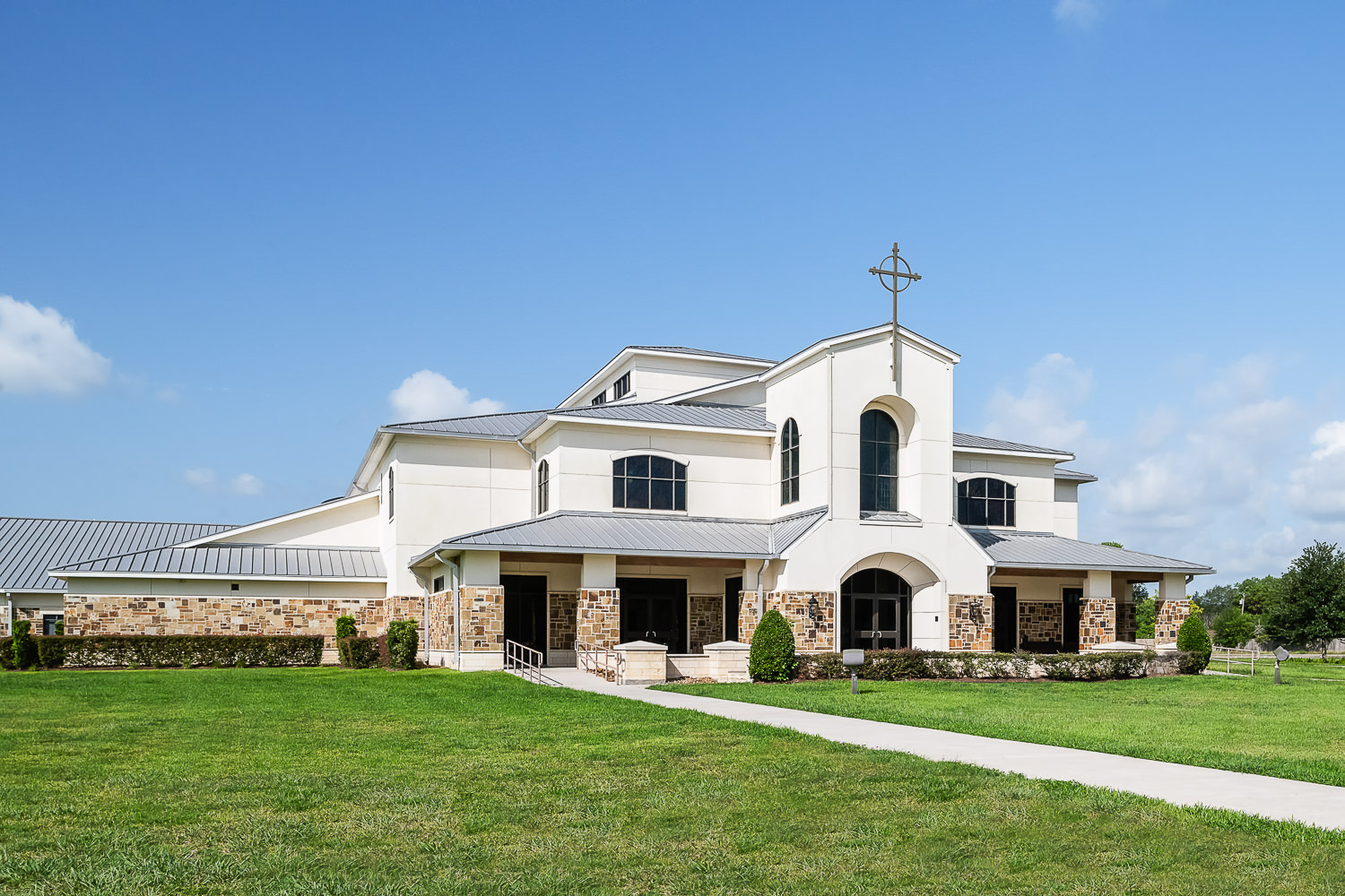 Architectural photo of the front exterior of Friendswood United Methodist Church, a large institutional building, pictured on a clear, sunny day.