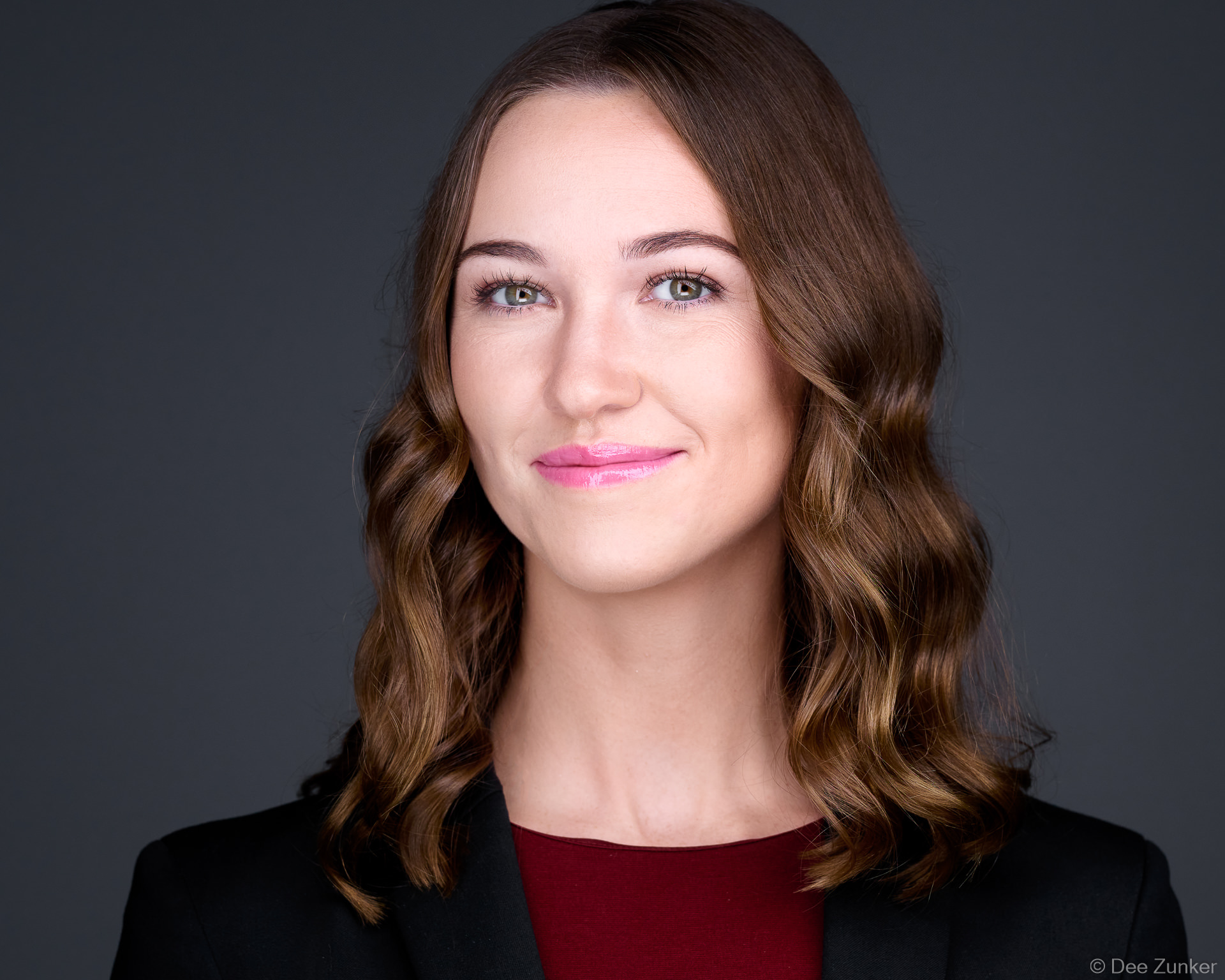 Professional woman in black blazer and burgundy top poses for a corporate headshot, styled for executive portraits or annual report photography in Houston.