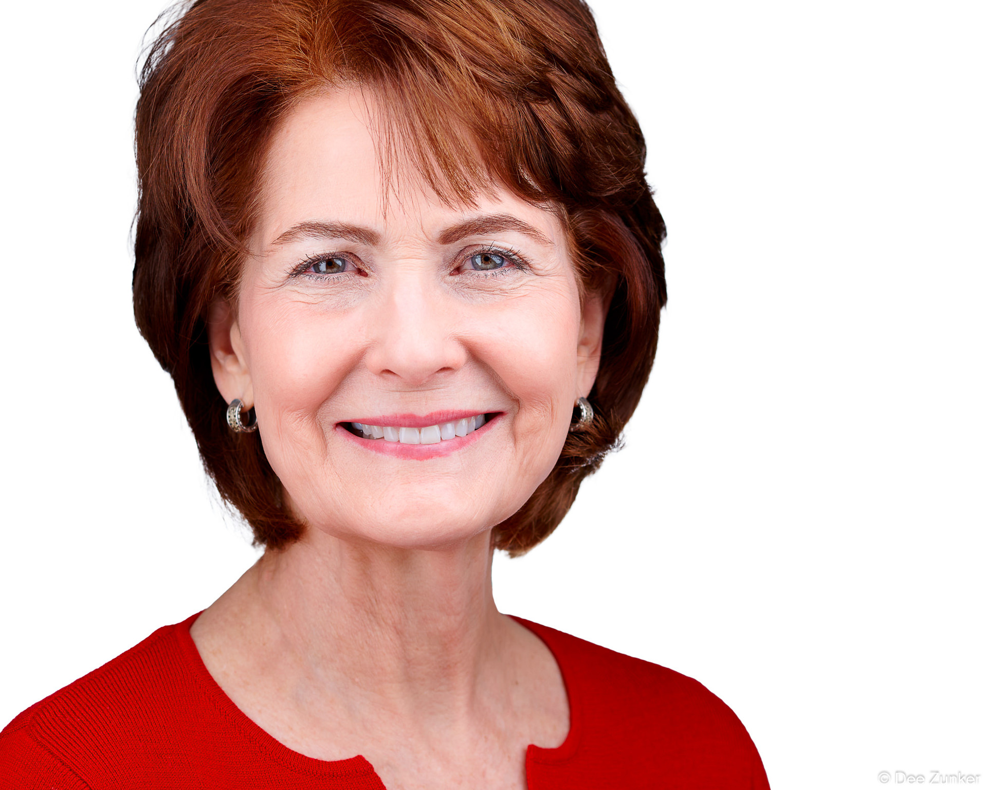 Smiling professional woman with auburn hair wearing a red top, corporate headshot portrait taken at Houston photography studio.