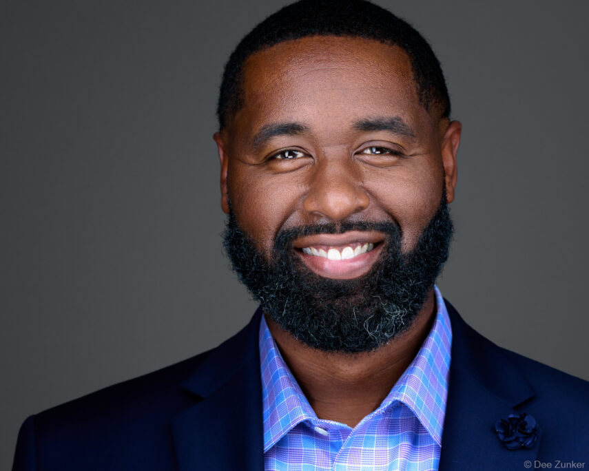 Smiling man with beard in navy blazer and plaid shirt, professional corporate headshot, Houston TX studio photography.