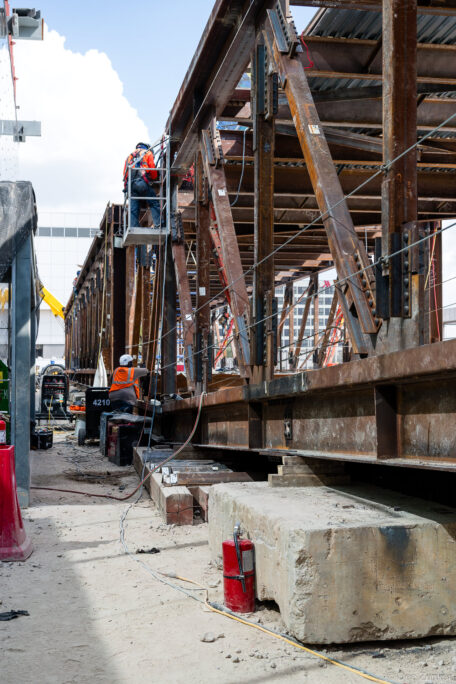 Construction workers in safety harnesses work on large weathered steel truss structure during IAH Terminal B structural framing, Houston.