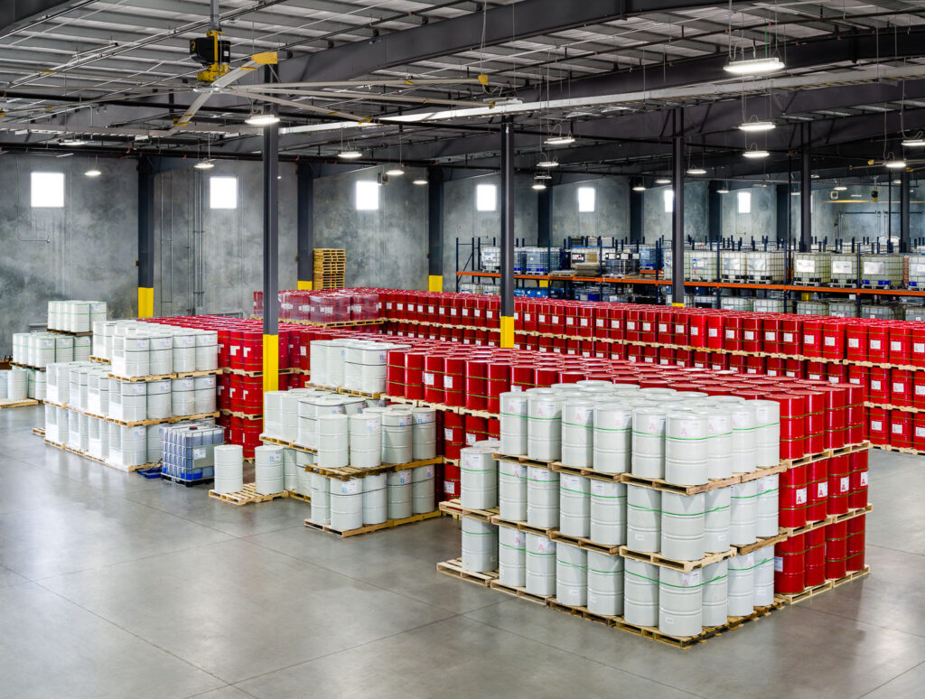 Elevated drone shot in an industrial warehouse. Red and white drums are stacked neatly in organized rows, showing logistics storage.