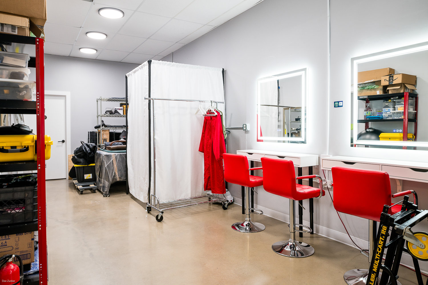 Professional hair and makeup area featuring dual lighted vanity mirrors, wardrobe racks, and a private changing booth for headshot and branding sessions. - Home of Dee Zunker Photography