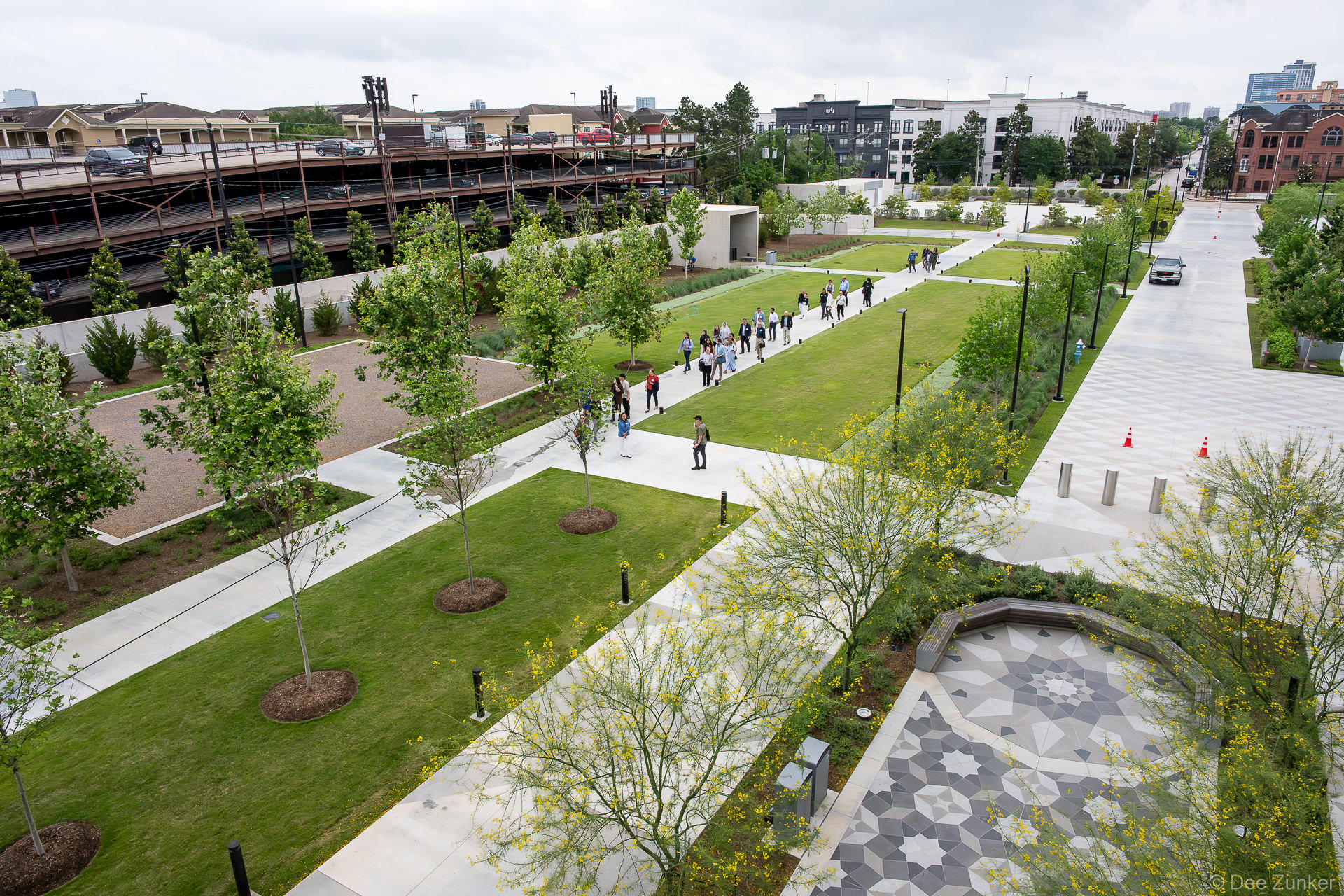 Elevated view of The Ismaili Center Houston grounds along Allen Parkway, with conference attendees walking geometric pathways amid green lawns and young trees.