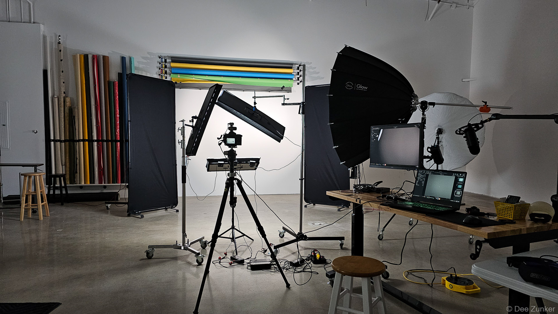 Professional photography studio in Houston with softbox lighting, camera on tripod, tethered laptop, and colorful backdrop paper rolls.