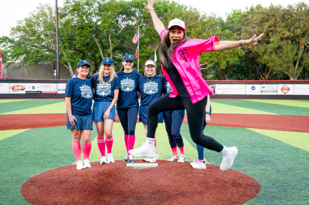 Women in Moms Coach shirts pose on the pitcher's mound at Weston Field during a Bellaire Little League American League game.