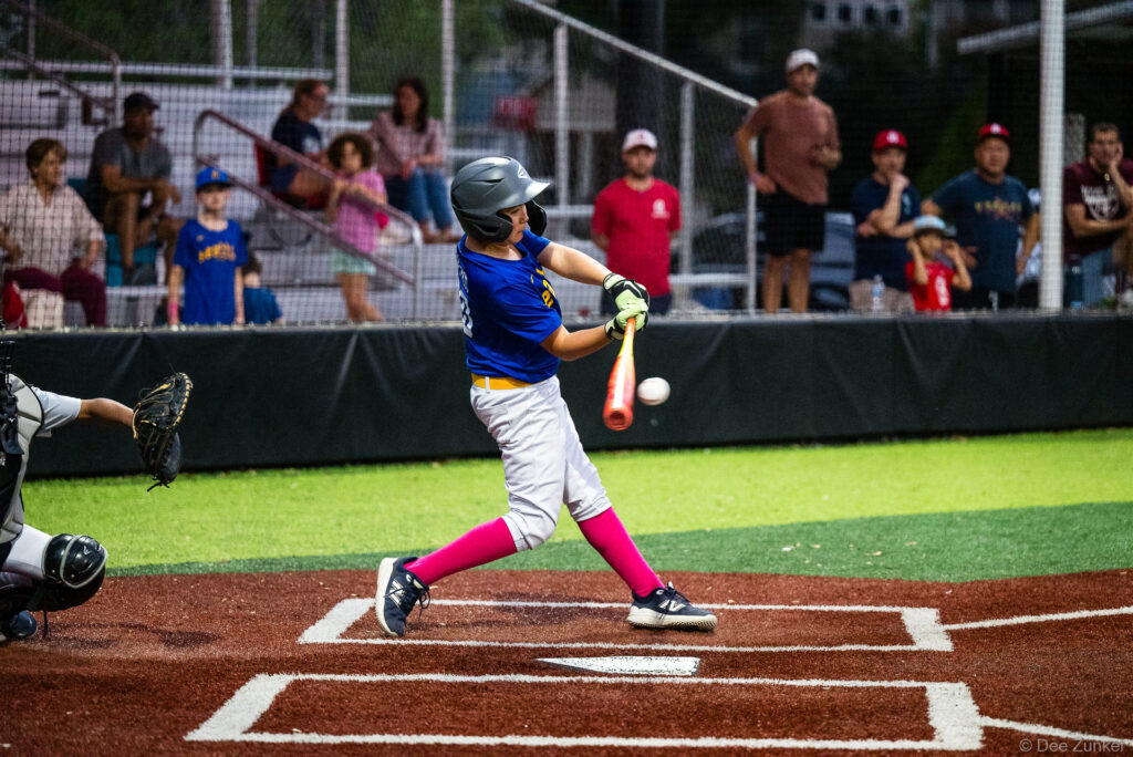 Young Mariners batter makes contact at home plate during a Bellaire Little League American League game at Weston or Tiras Field in Bellaire TX.