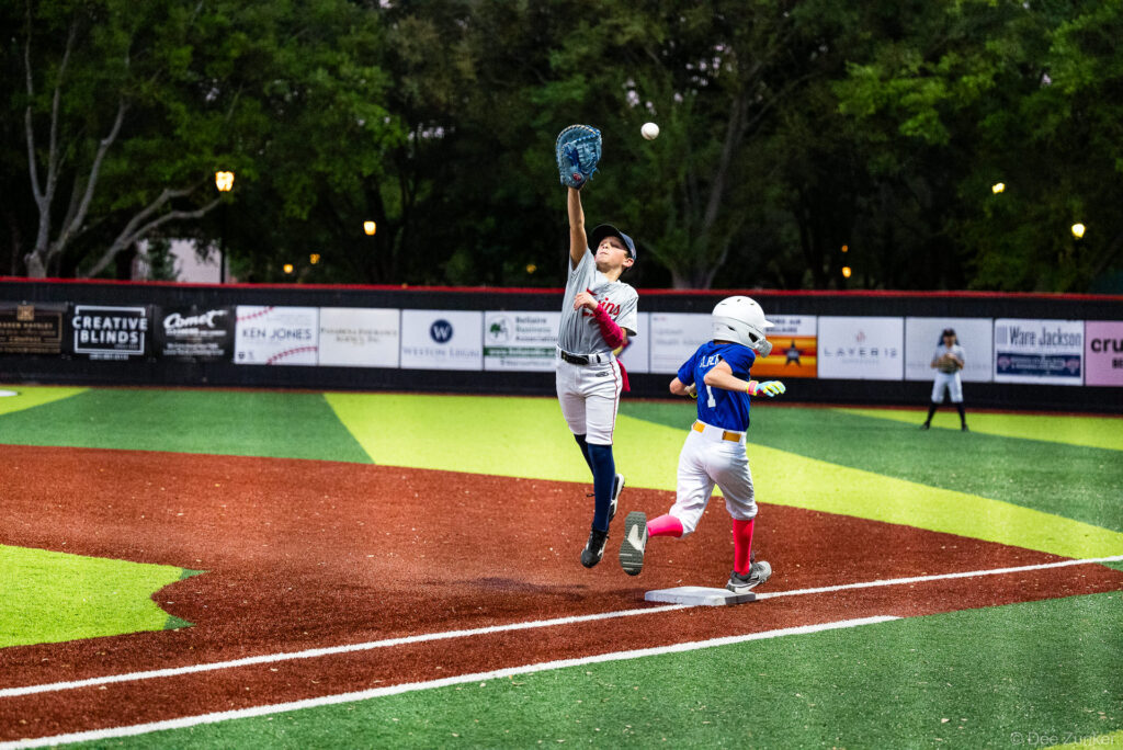 Bellaire Little League Twins first baseman leaps to catch a high throw at first base as a Mariners runner rounds the bag at Weston Field.
