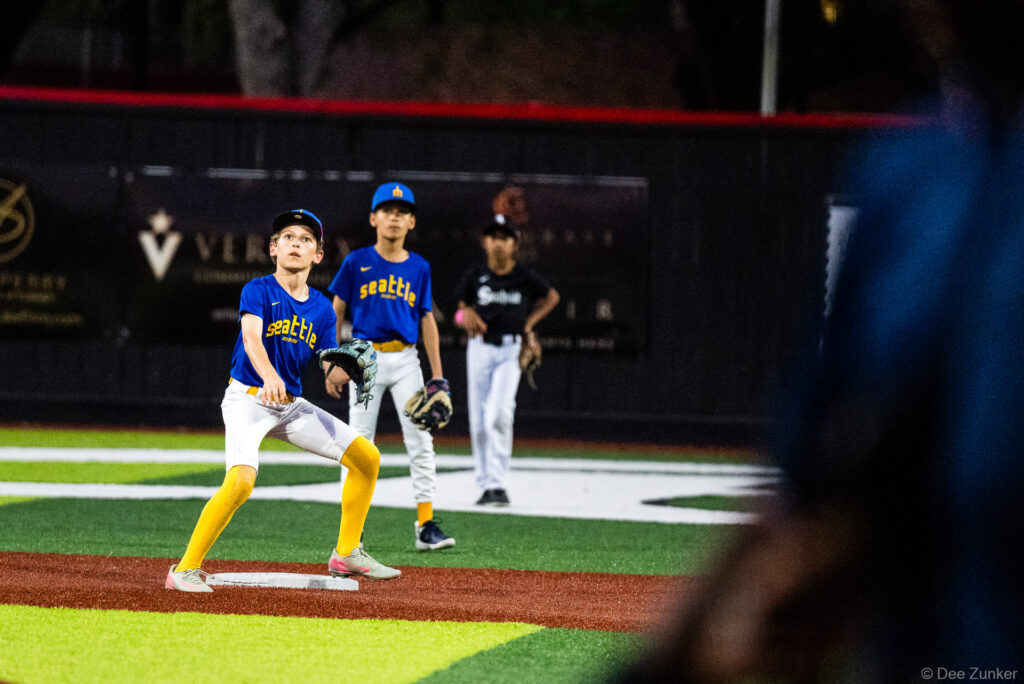 Young Seattle Mariners fielder tracks a fly ball at first base during a Bellaire Little League American League game at Weston Field in Bellaire TX.