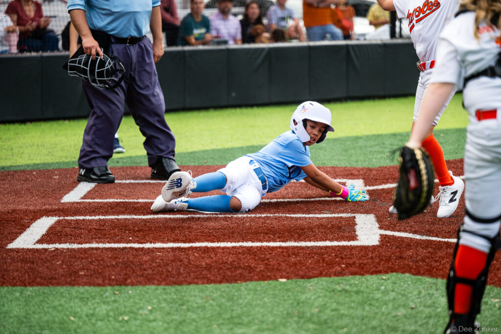 Rays baserunner slides headfirst into home plate as Orioles catcher awaits the ball during Bellaire Little League action at Weston Field, Bellaire TX.