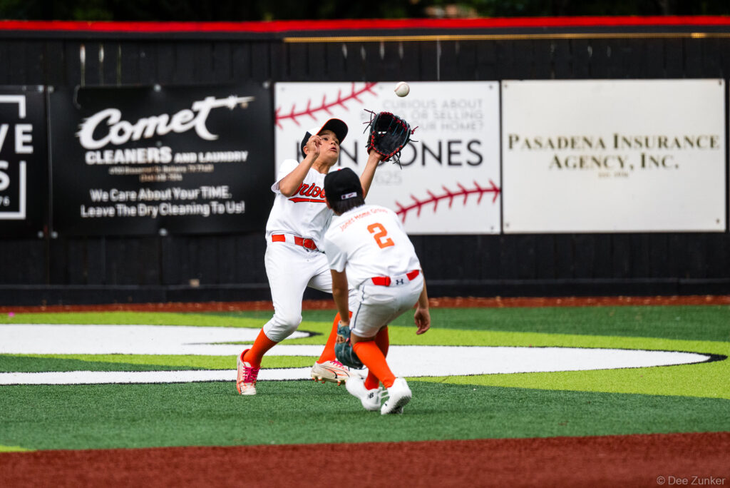 Two Bellaire Little League Orioles players nearly collide tracking a fly ball during an American League game at Weston or Tiras Field in Bellaire TX.
