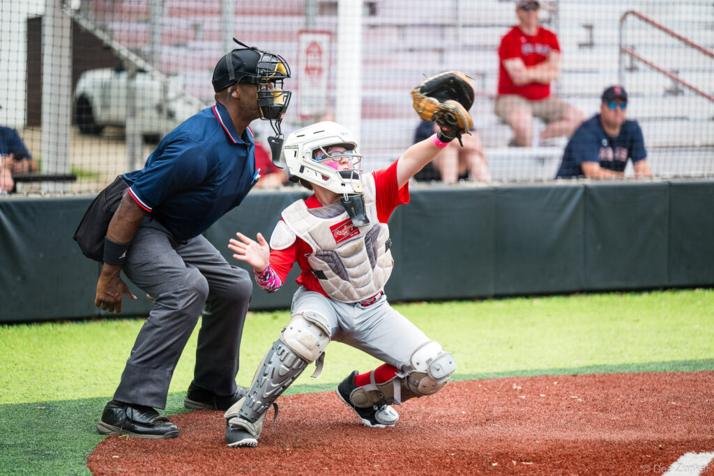 Red Sox catcher in full gear reaches to frame a pitch at home plate as the umpire looks on, Bellaire Little League American League game.