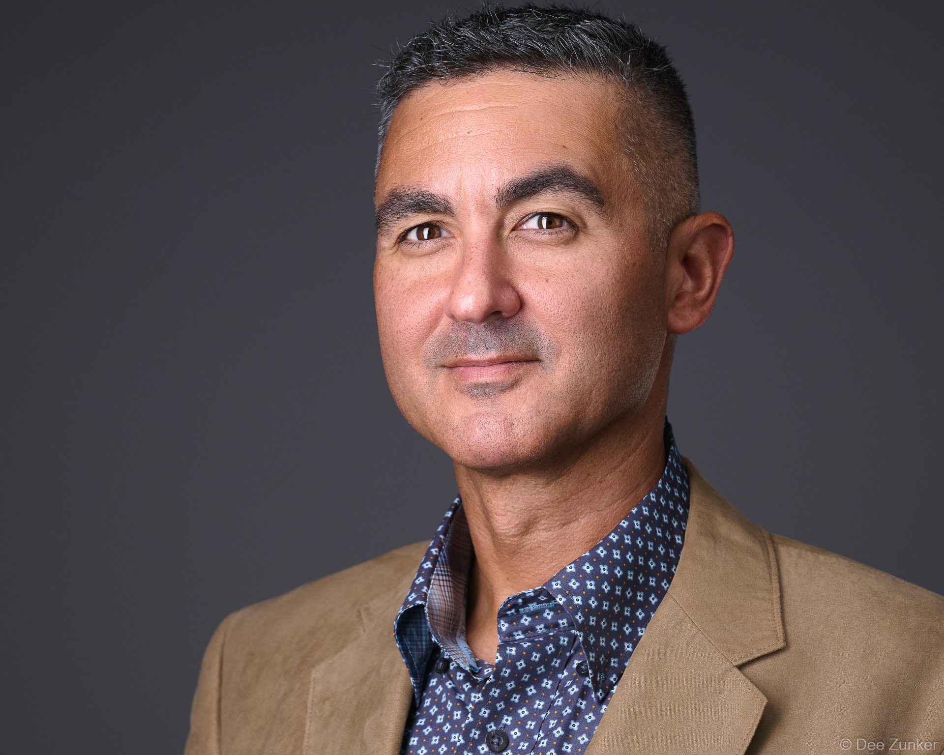Male executive in tan blazer and patterned shirt, confident expression, professional studio headshot with neutral gray backdrop, Houston.