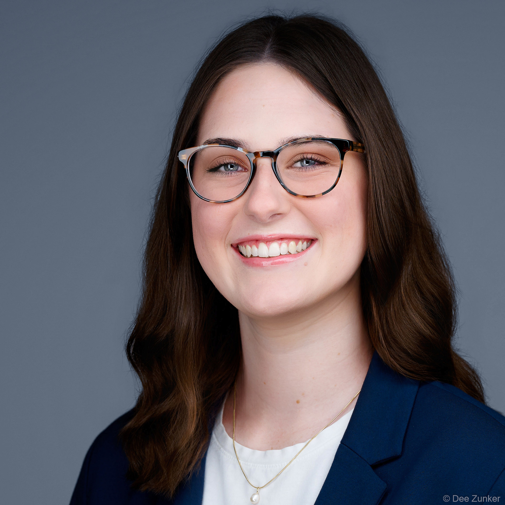 Smiling professional woman in navy blazer and glasses, studio headshot on neutral gray backdrop, Houston corporate portrait photography.