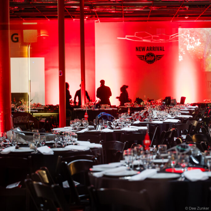 Red-lit event hall at The Shop Club Houston with round banquet tables set for the 40th Annual AIA Houston Design Gala.