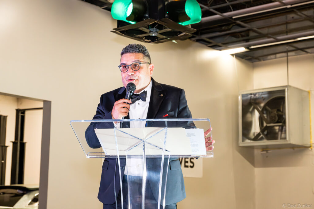Man in tuxedo speaks at clear acrylic podium during 40th Annual AIA Houston Design Gala at The Shop Club Houston.