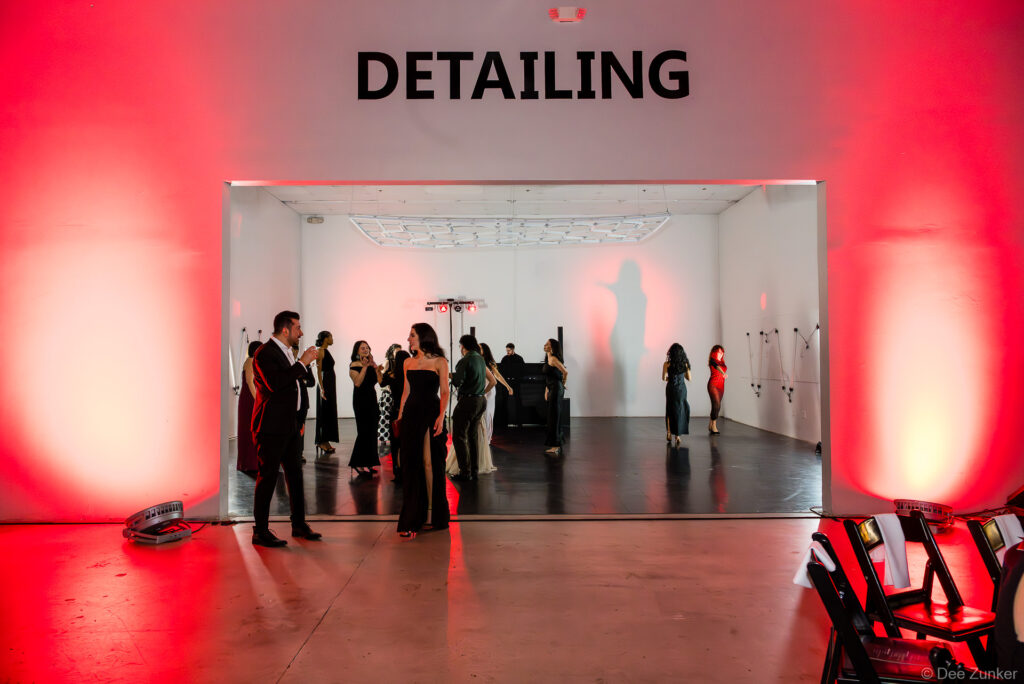 Formally dressed guests mingle inside a white auto detailing bay with red uplighting at the 40th Annual AIA Houston Design Gala.