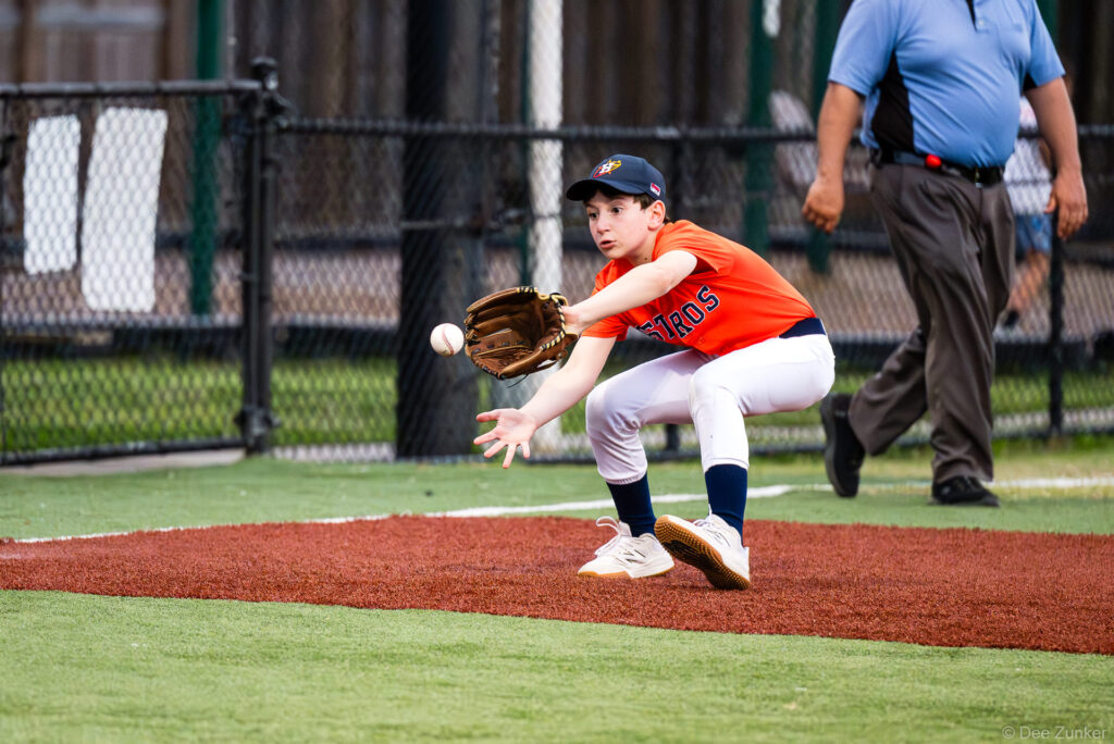 Young Astros infielder crouches to field a ground ball at Bellaire Little League game, Weston or Tiras Field, Bellaire TX.