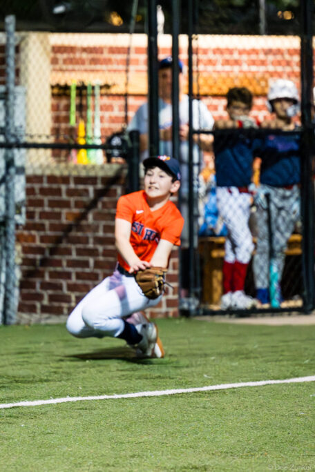 Young Astros fielder drops to a knee to make a low catch during a Bellaire Little League American League game at Weston or Tiras Field, Bellaire TX.