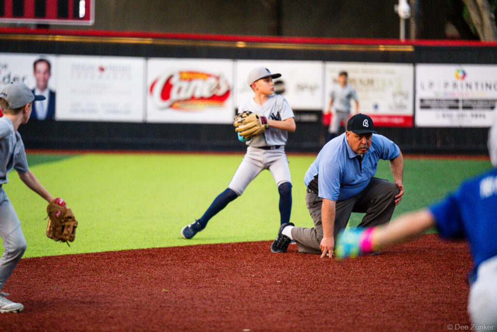 Youth baseball infielder throws to first as an umpire watches closely during a Bellaire Little League American League game at Weston Field.