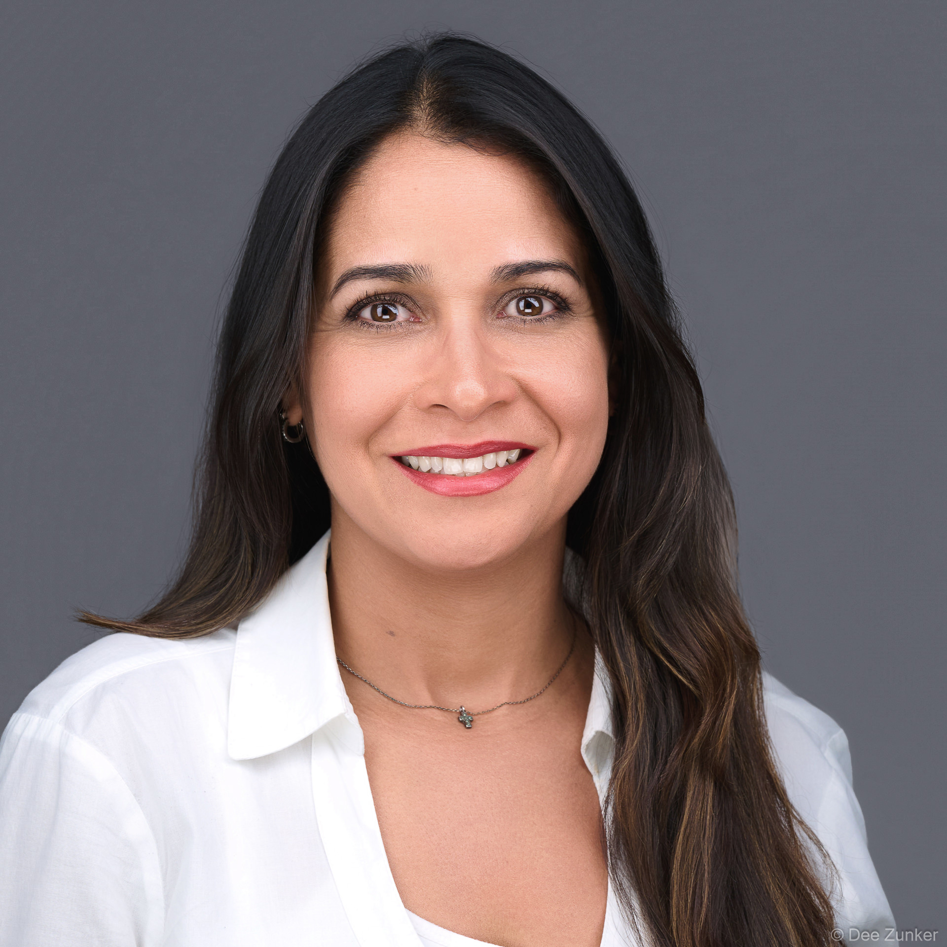 Professional woman in white blouse smiles warmly against a gray backdrop in a Houston studio headshot session with soft 3-point lighting.