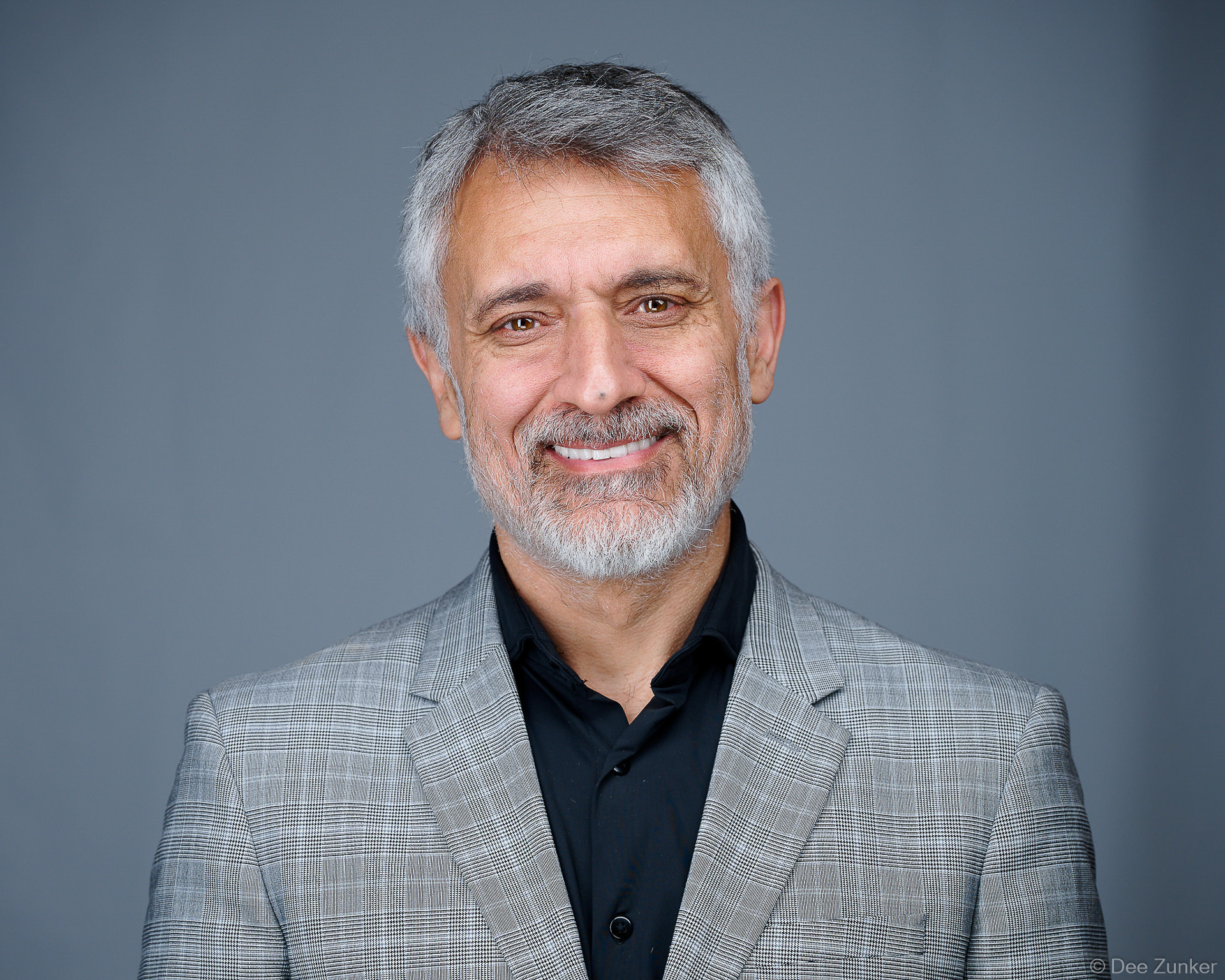 Smiling middle-aged man with gray hair and beard wearing a gray blazer, photographed at a Houston sponsor activation headshot booth.