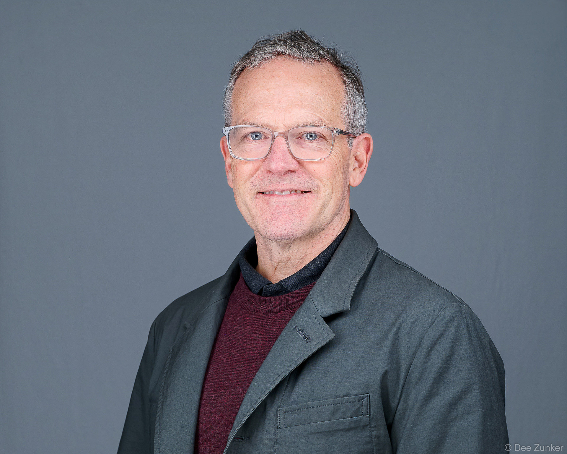Smiling middle-aged man with glasses in gray jacket, photographed at a Houston trade show event headshot booth activation.