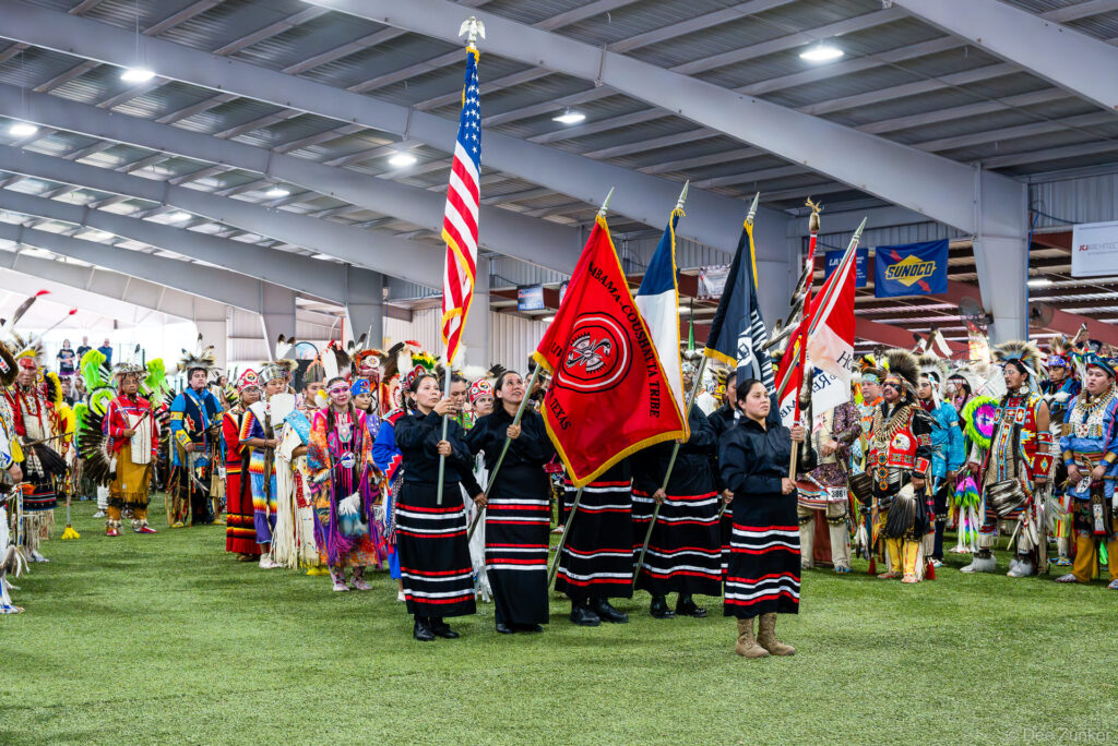 Alabama-Coushatta Tribe color guard carries flags during Grand Entry at the 56th Annual Powwow in Texas, surrounded by dancers in regalia.