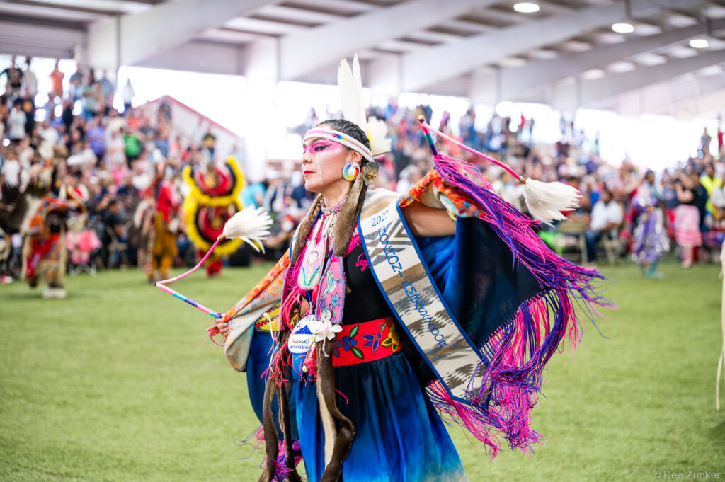 Native American woman dancer in colorful regalia with feathers and sash performs at Alabama-Coushatta 56th Annual Powwow Texas