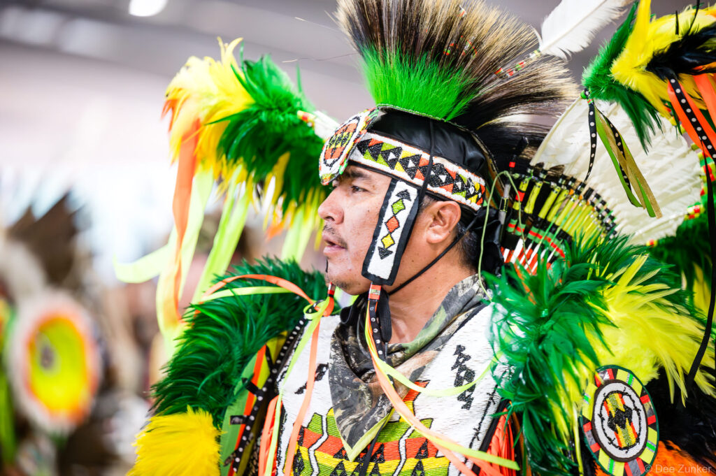 Native American male dancer in vibrant green and yellow feathered regalia and beaded headdress at Alabama-Coushatta Powwow Grand Entry Texas