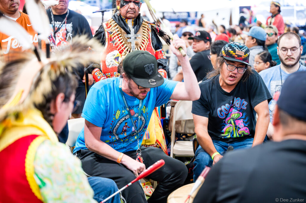 Drummers playing at the Alabama-Coushatta 56th Annual Powwow in Texas, with traditional regalia visible in the background.