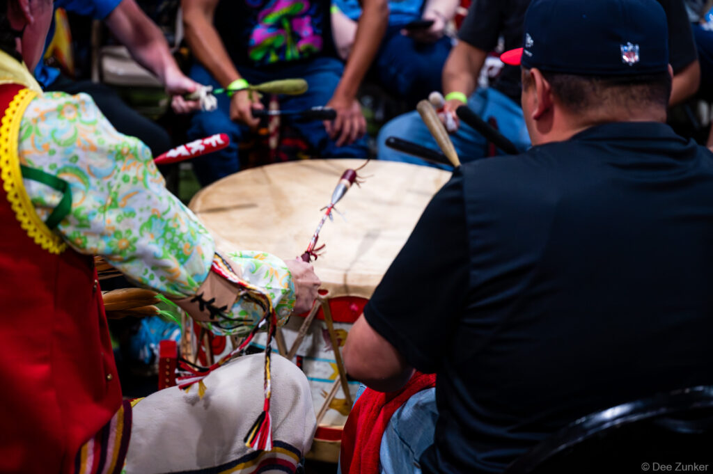 Drummers gathered around a large ceremonial drum at the Alabama-Coushatta 56th Annual Powwow in Texas, striking with decorated beaters.
