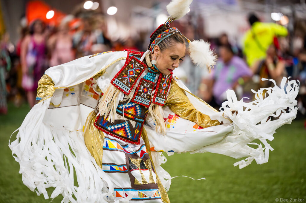 Native American woman dancer in white fringed regalia and beaded vest performs at Alabama-Coushatta 56th Annual Powwow, Texas