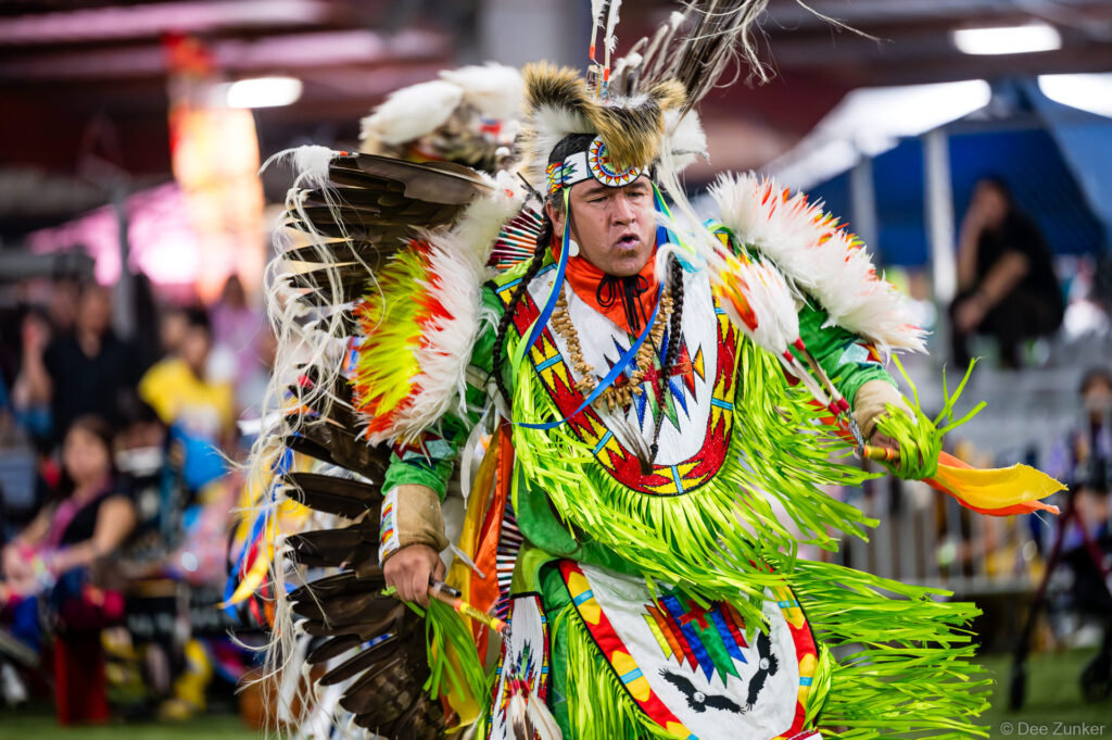 Male fancy dancer in vibrant green fringe and feather regalia performing at the Alabama Coushatta 56th Annual Powwow in Texas