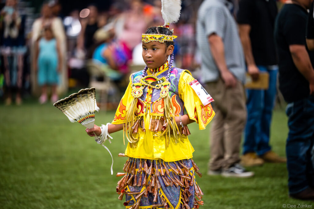 Young Native American girl in jingle dress regalia holding feather fan at Alabama-Coushatta 56th Annual Powwow Texas 2026