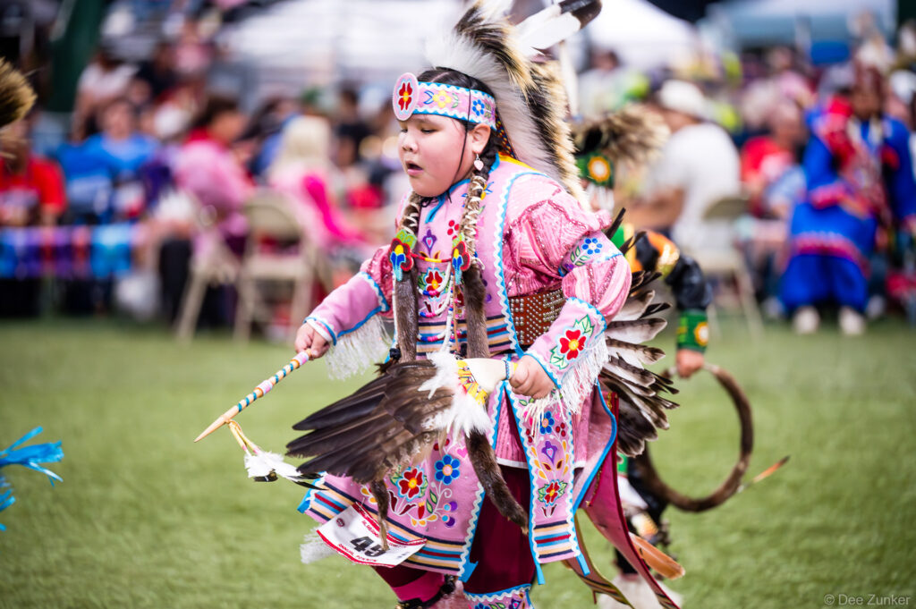 Young girl in beaded pink regalia dances at the Alabama-Coushatta 56th Annual Powwow, Texas, holding eagle feather fan.