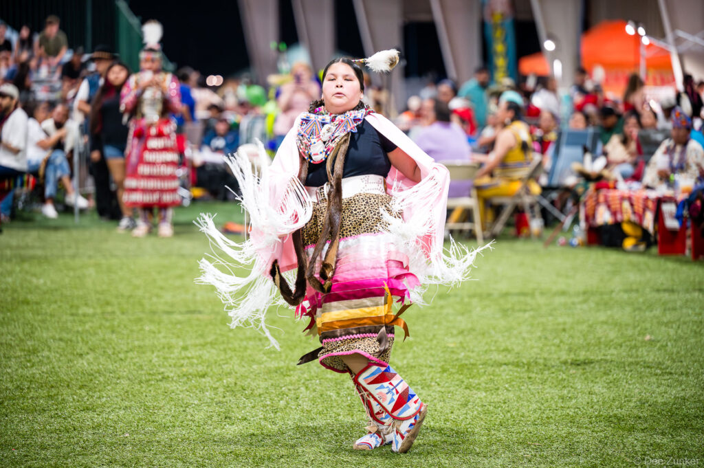 Young Native American dancer in traditional regalia with white fringe shawl and beaded moccasins performing at Alabama Coushatta Powwow Texas