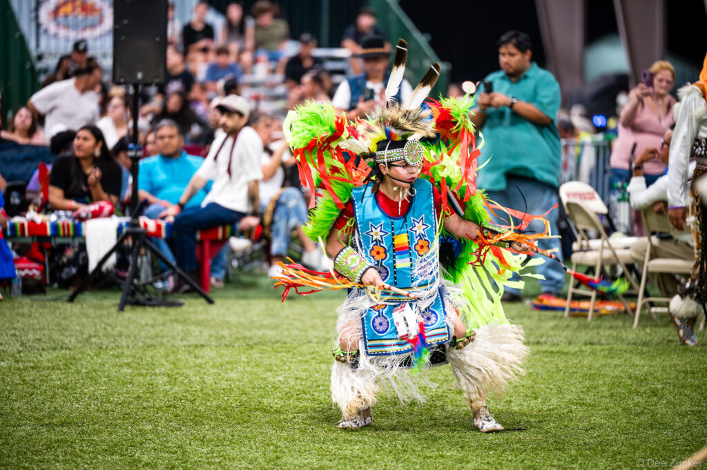 Young male fancy dancer in vibrant blue regalia with neon feathers performs at Alabama-Coushatta 56th Annual Powwow, Texas