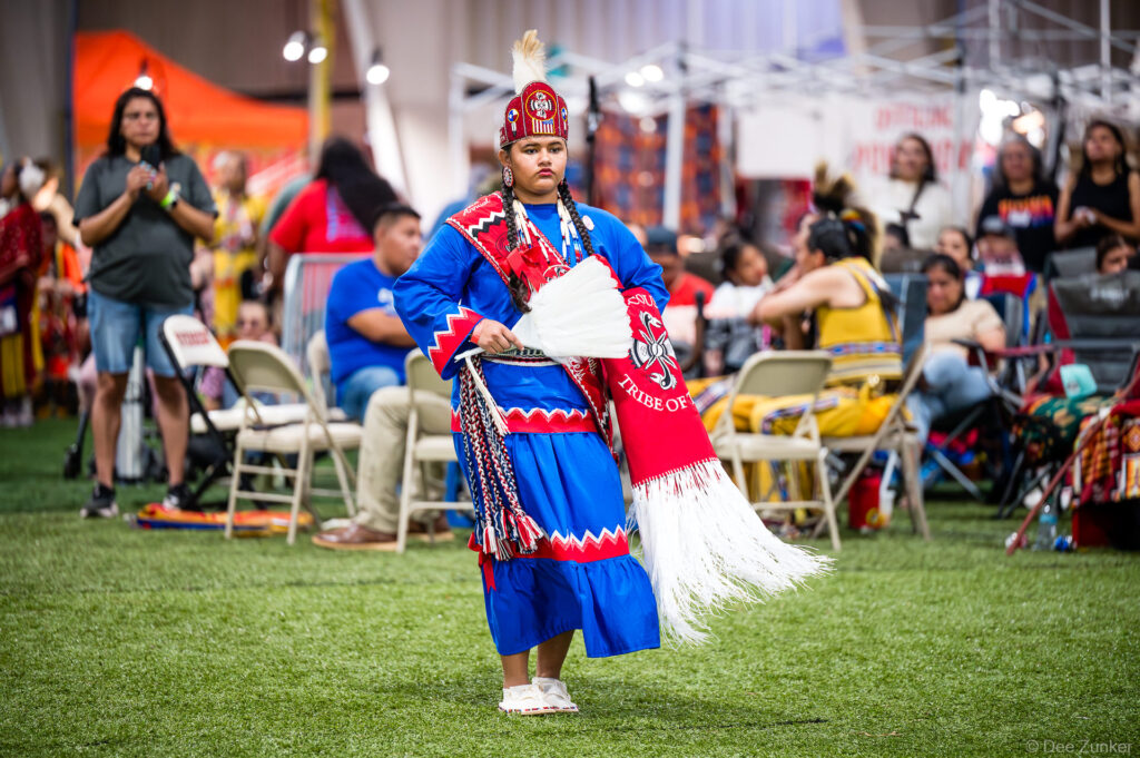 Young Native American girl in blue and red regalia holds white feather fan while dancing at Alabama-Coushatta 56th Annual Powwow Texas