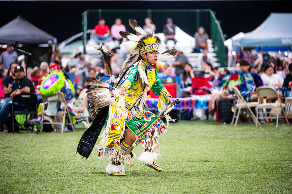 Native American dancer in vibrant yellow regalia and feathered headdress performing at the Alabama-Coushatta 56th Annual Powwow in Texas.