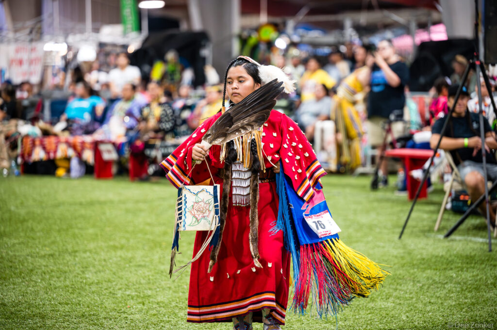 Young Native American dancer in red regalia holding eagle feathers performs at Alabama-Coushatta 56th Annual Powwow, Texas