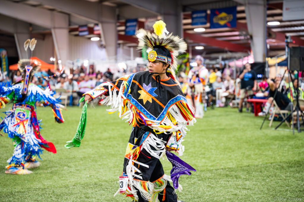 Native American dancer in black regalia with colorful fringe and feathered headdress performs at Alabama-Coushatta 56th Annual Powwow Texas