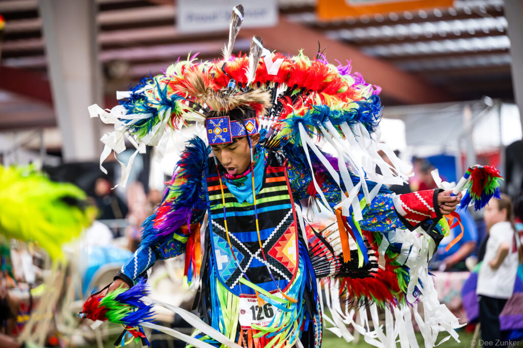 Male fancy dancer in vibrant feathered regalia performs at the Alabama-Coushatta 56th Annual Powwow, Texas, June 2026.